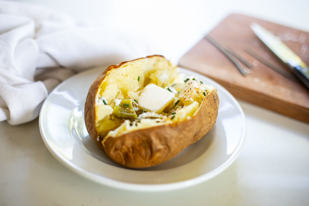 baked potato on plate with butter, yogurt, chives, salt, and pepper