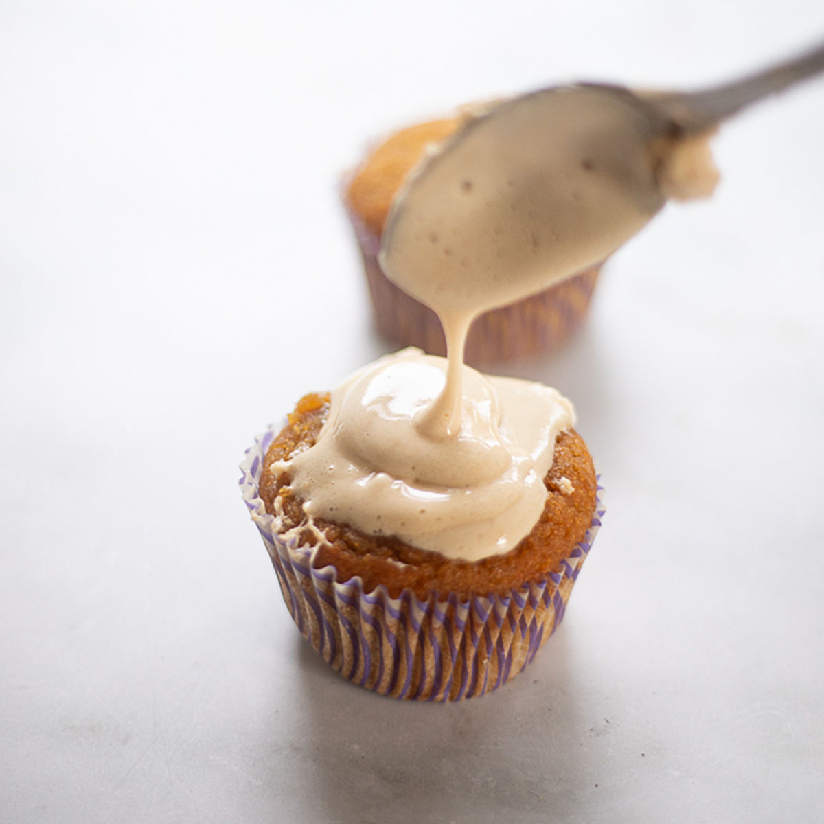 marshmallow frosting being drizzled on vanilla cupcake